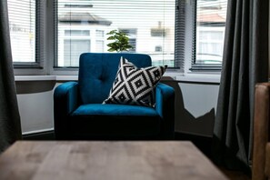 A blue armchair with a patterned pillow, positioned near a window with blinds, and a wooden table in front. - 2 bed house near Devonport Dockyard Plymouth (Plymouth)