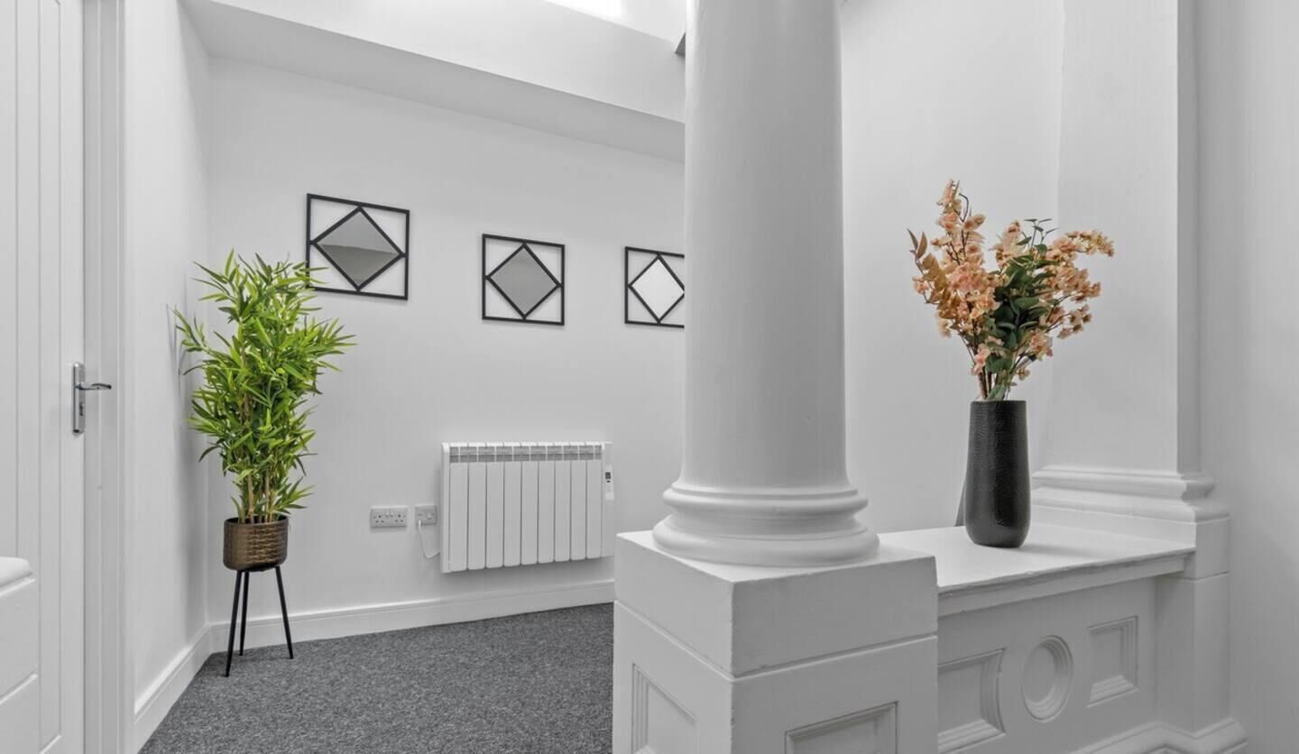 Un couloir avec un radiateur, une plante en pot et un vase rempli de fleurs.