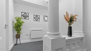 A hallway with a radiator, a potted plant, and a vase with flowers. - Modern 2 bed Plymouth apartment with city views (Plymouth)