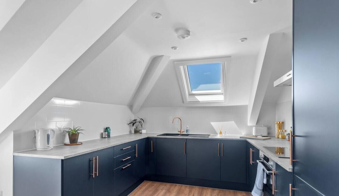 Une cuisine moderne avec des meubles de couleur sombre, un puits de lumière et un plan de travail blanc.