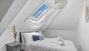 Ein Schlafzimmer mit Dachfenster, einem Bett mit weißer Bettwäsche, einem Nachttisch mit einer Vase und einem Handtuch auf dem Bett.