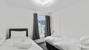 Habitación de hotel con dos camas, una ventana con cortinas, una puerta y una lámpara con forma de corazón.