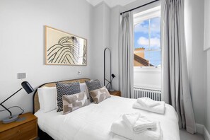 A hotel room with a bed, bedside lamps, a window with curtains, a radiator, and a framed artwork on the wall. - Sancroft by Pureserviced (Plymouth)