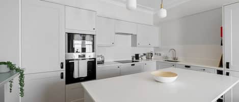 A modern kitchen with white cabinetry, a central island, a built-in oven, and pendant lighting.