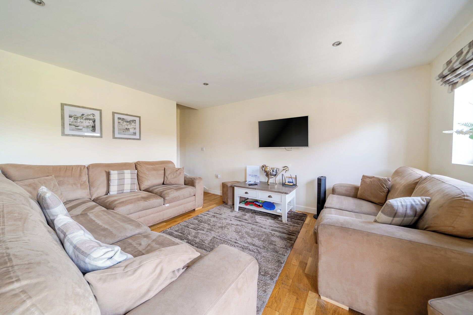 A living room with two beige sofas, a coffee table, a flat-screen TV, and a small white cabinet with drawers.