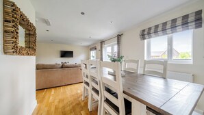 A dining area with a wooden table and white chairs, a sofa, and a TV mounted on the wall. - Lodge 13 - Hazelnut (Brigg)