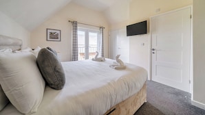 A bedroom with a bed, pillows, a TV, a door, and a window with curtains. - Lodge 13 - Hazelnut (Brigg)
