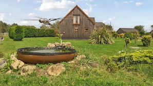 A wooden house with a triangular roof, a pond with rocks, and a garden with various plants. - Lodge 13 - Hazelnut (Brigg)