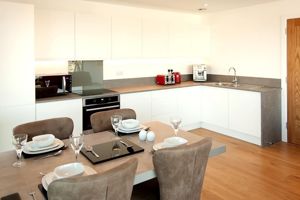 A modern kitchen with white cabinets, a dining table set with plates and glasses, and a coffee maker.