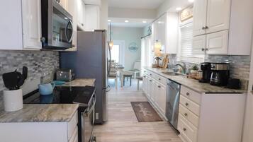 Una cocina moderna con armarios blancos, microondas, refrigerador, cafetera y un comedor al fondo.