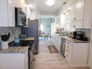 Eine moderne Küche mit weißen Schränken, einer Mikrowelle, einem Kühlschrank, einer Kaffeemaschine und einem Essbereich im Hintergrund.