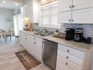 A modern kitchen with white cabinets, a stainless steel dishwasher, a coffee maker, and a wooden cutting board.