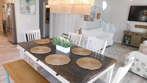 Et spiseområde med et mørkt træbord, hvide stole, vævede servietringe og en hængende lampe.