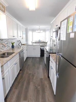 A kitchen with white cabinets, a stainless steel refrigerator, and a granite countertop. - Ocean Lakes 1028, 5 Bdrm/4 Bath near ocean Golf Cart (Myrtle Beach)
