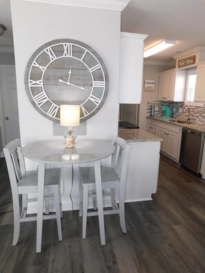 A dining area with a round table, four chairs, a large wall clock, and a small lamp. - Ocean Lakes 1028, 5 Bdrm/4 Bath near ocean Golf Cart (Myrtle Beach)