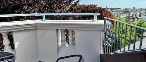 A balcony with a chair, railing, and a view of a cityscape.
