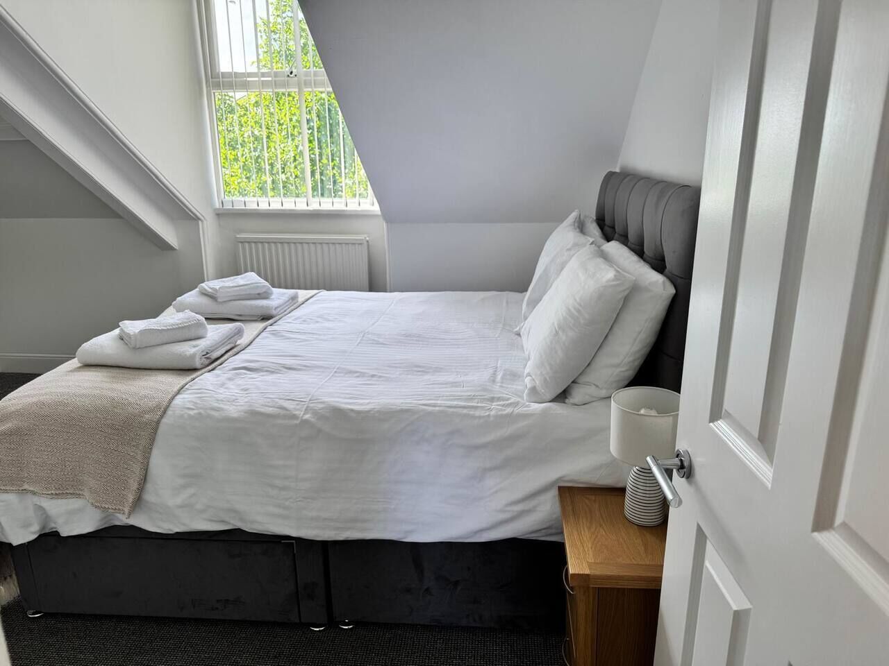 A bedroom with a bed, a bedside table, a window, and a door.