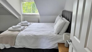 Un dormitorio con cama, mesita de noche, ventana y puerta.