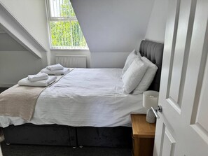 Une chambre à coucher avec un lit, une table de chevet, une fenêtre et une porte.
