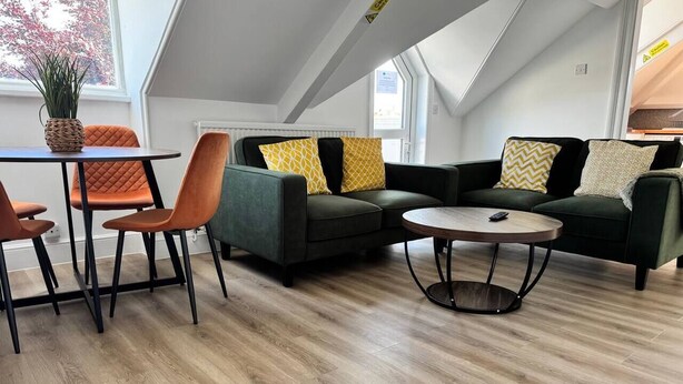 Un moderno espacio tipo loft con techo alto, un comedor con mesa y sillas, un conjunto de sofás y una mesa de centro redonda.