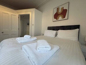 A hotel room with a large bed, two rolled towels, a headboard, a nightstand, and a framed artwork on the wall. - 2 bed Lower Deck Wilderness Hse by Smart Welcomes (Plymouth)