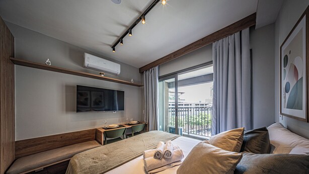 Une chambre d’hôtel moderne dotée d’un grand lit, d’un bureau, d’une télévision à écran plat et d’un balcon avec des rideaux.