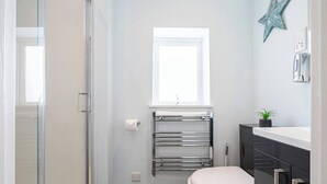 Ein Badezimmer mit Duschkabine, Toilette, Handtuchhalter, kleinem Fenster und Waschbecken mit Pflanze.