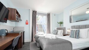 A hotel room with a bed, a desk, a chair, a TV, and a window with curtains. - Twin @ Ocean Stays by Smart Welcomes (Plymouth)