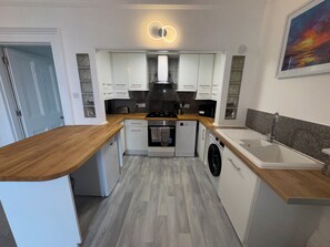 A compact kitchen with a wooden countertop, built-in appliances, and a small sink. - 2 Bed - The Poop Deck by Smart Welcomes (Plymouth)