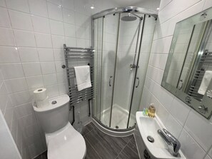 Een moderne badkamer met toilet, een douche met glazen wanden, een wastafel en een spiegel.