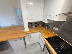 Een kleine keuken met witte kastjes, een houten aanrechtblad, een inbouwfornuis en een kleine koelkast.
