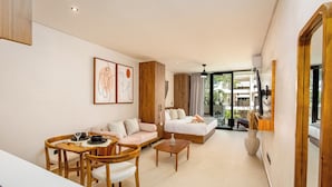 Una habitación de hotel moderna con zona de comedor, sofá, cama y un ventanal grande.