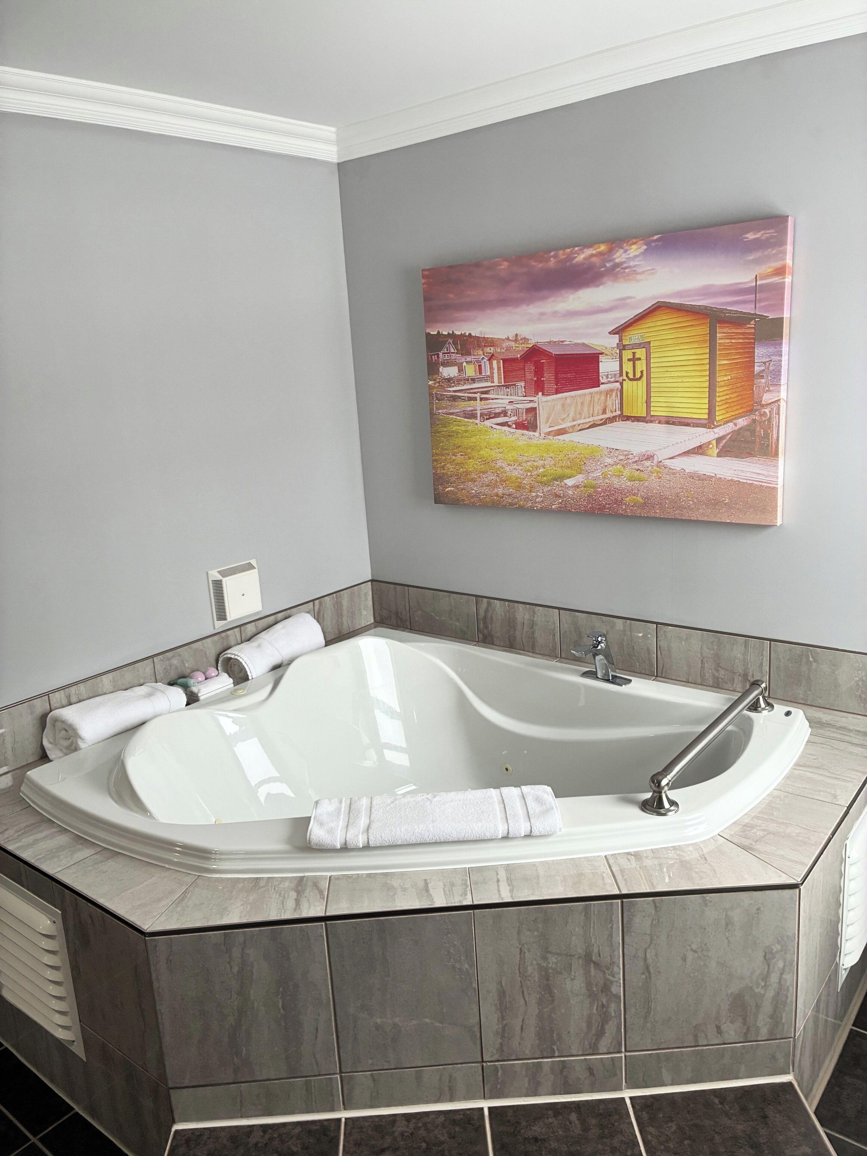 Une salle de bain moderne avec une baignoire sur pieds, un porte-serviettes et un tableau représentant un paysage côtier.