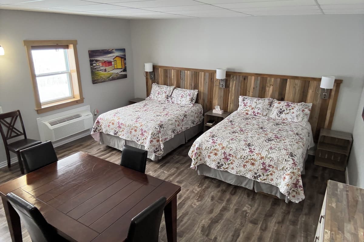 Habitación de hotel con dos camas, cabecero de madera, una mesa de comedor y ventana con vistas.