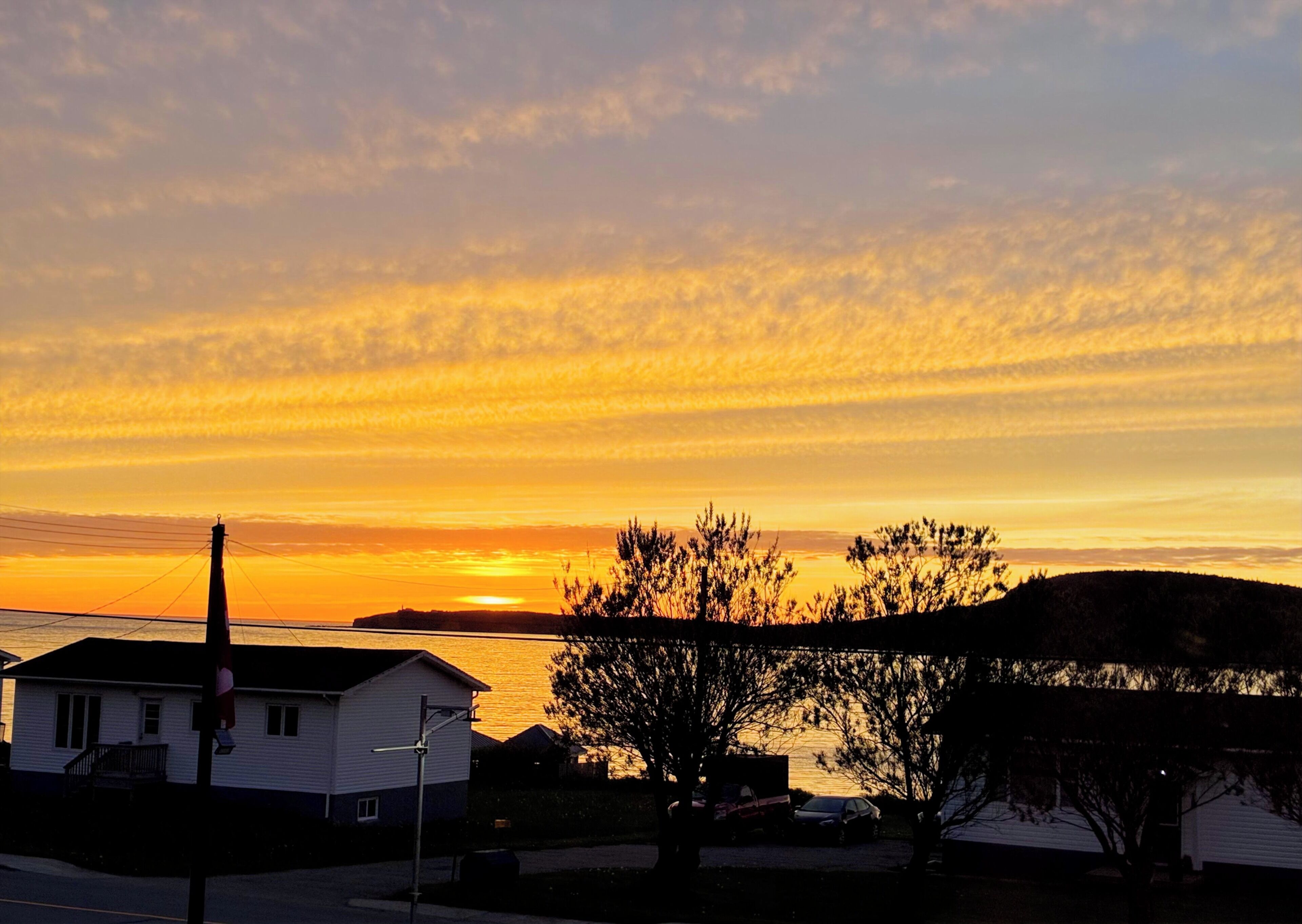 Una vista al atardecer sobre una masa de agua, con casas y árboles en primer plano.