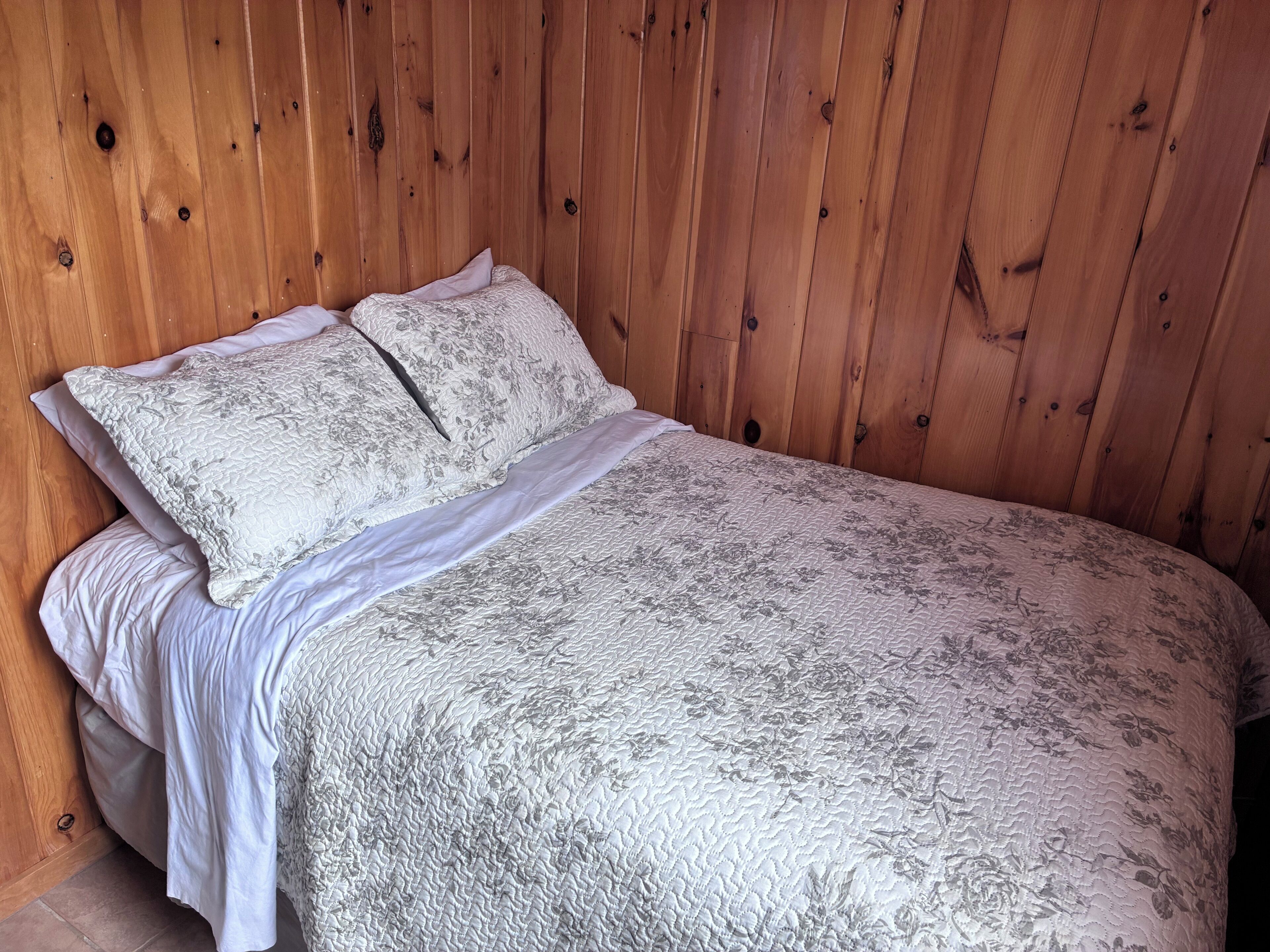 A bed with a floral-patterned bedspread and two pillows, set against a wooden wall.
