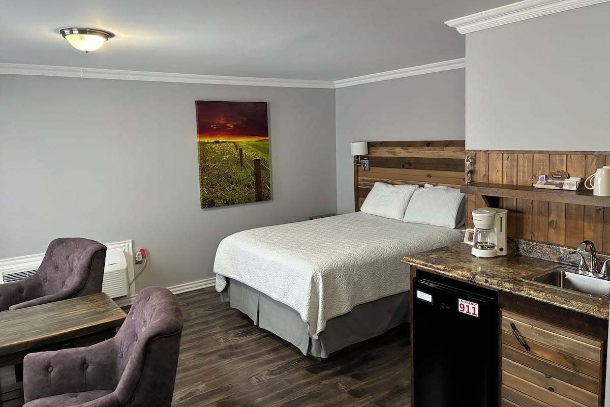 Un dormitorio con cama, mesita de noche, cafetera y lámpara de pared.