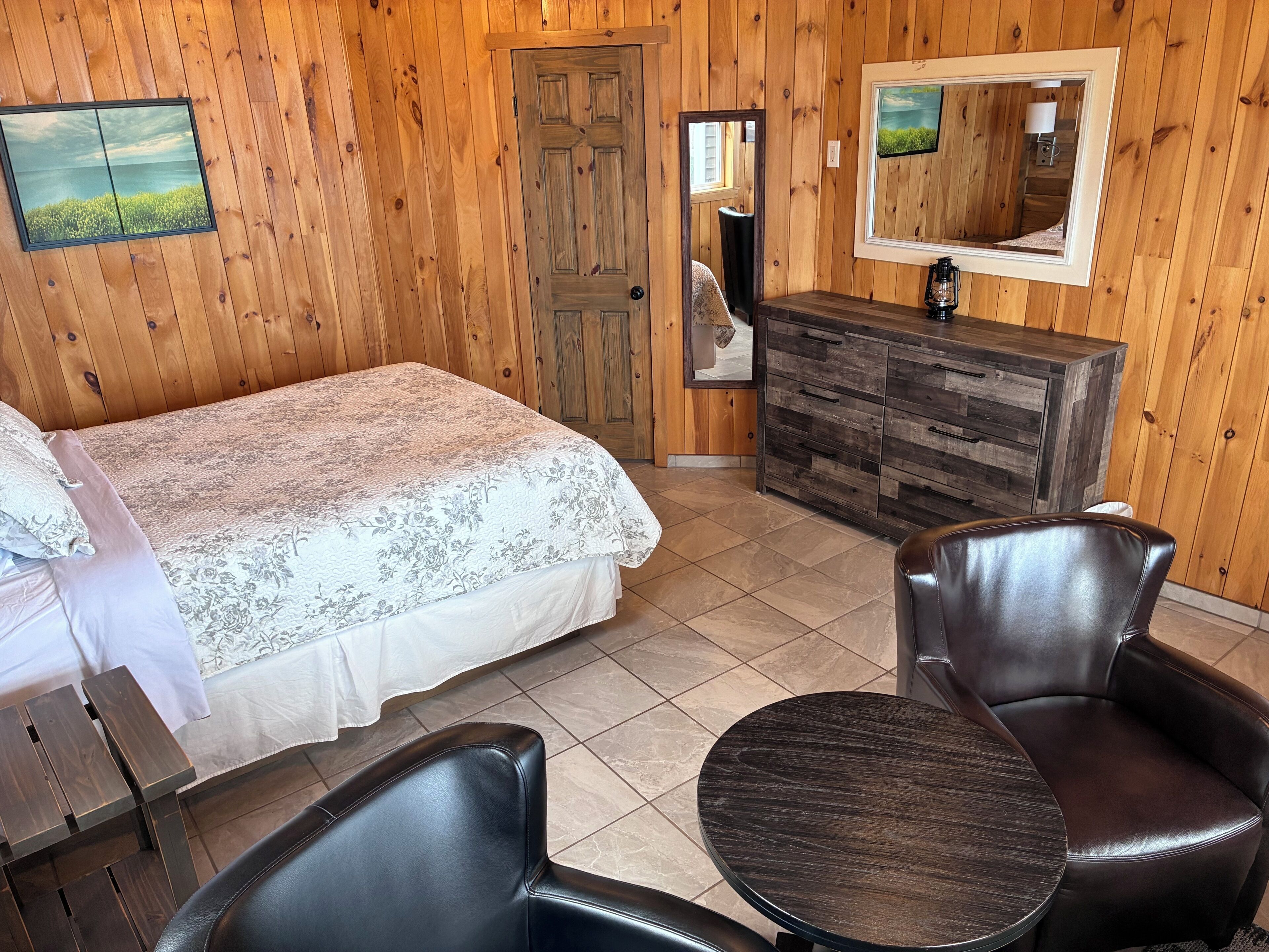 Ein Zimmer mit Holzwänden, einem Bett, einem Schminktisch, einem Spiegel, einem runden Tisch und zwei Stühlen.
