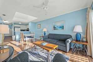 A living room with a sofa, coffee table, and chairs, a dining area with a table and chairs, and a kitchen in the background. - Pelican's Landing 316- 3BR In Shore Drive- Pool (Myrtle Beach)