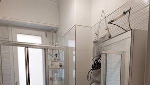Et moderne badeværelse med et glasbadeværelsesafskærmning, en hvid vask med spejl og diverse toiletartikler.