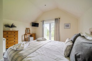 Une chambre à coucher avec un lit, une commode, un téléviseur et une fenêtre avec des rideaux.