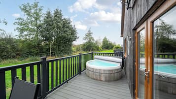 A wooden deck with a hot tub and a glass-enclosed room.