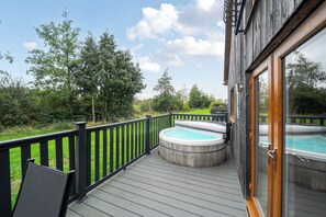 Une terrasse en bois avec un jacuzzi et une pièce fermée par des baies vitrées.