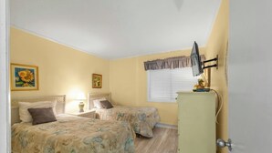 Habitación con dos camas, una mesita de noche con lámpara, cómoda y ventana con persianas.