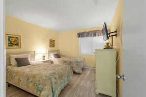 A room with two beds, a small table with a lamp, a dresser, and a window with blinds. - 3BR In Shore Drive- Pelican's Landing 326- Pool (Myrtle Beach)
