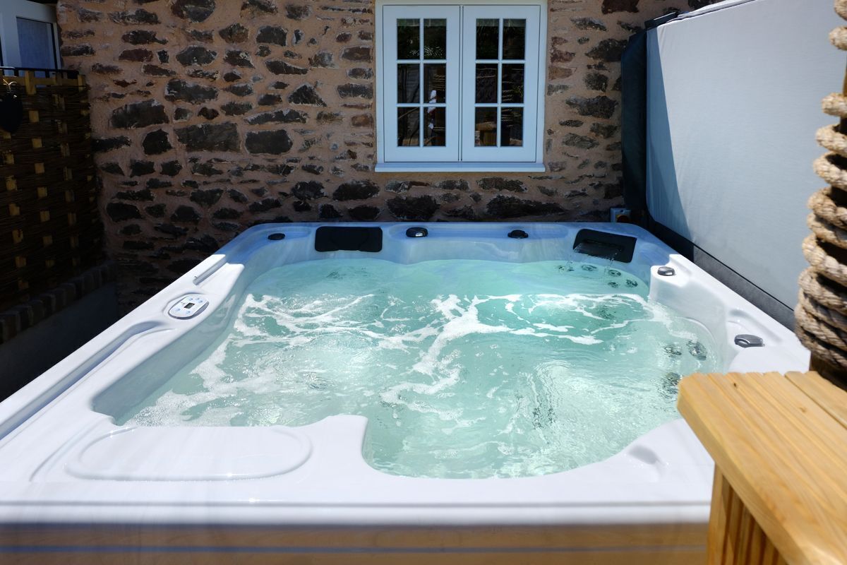 Un bain à remous dans un espace extérieur entouré de murs en pierre, avec une terrasse en bois et une fenêtre.