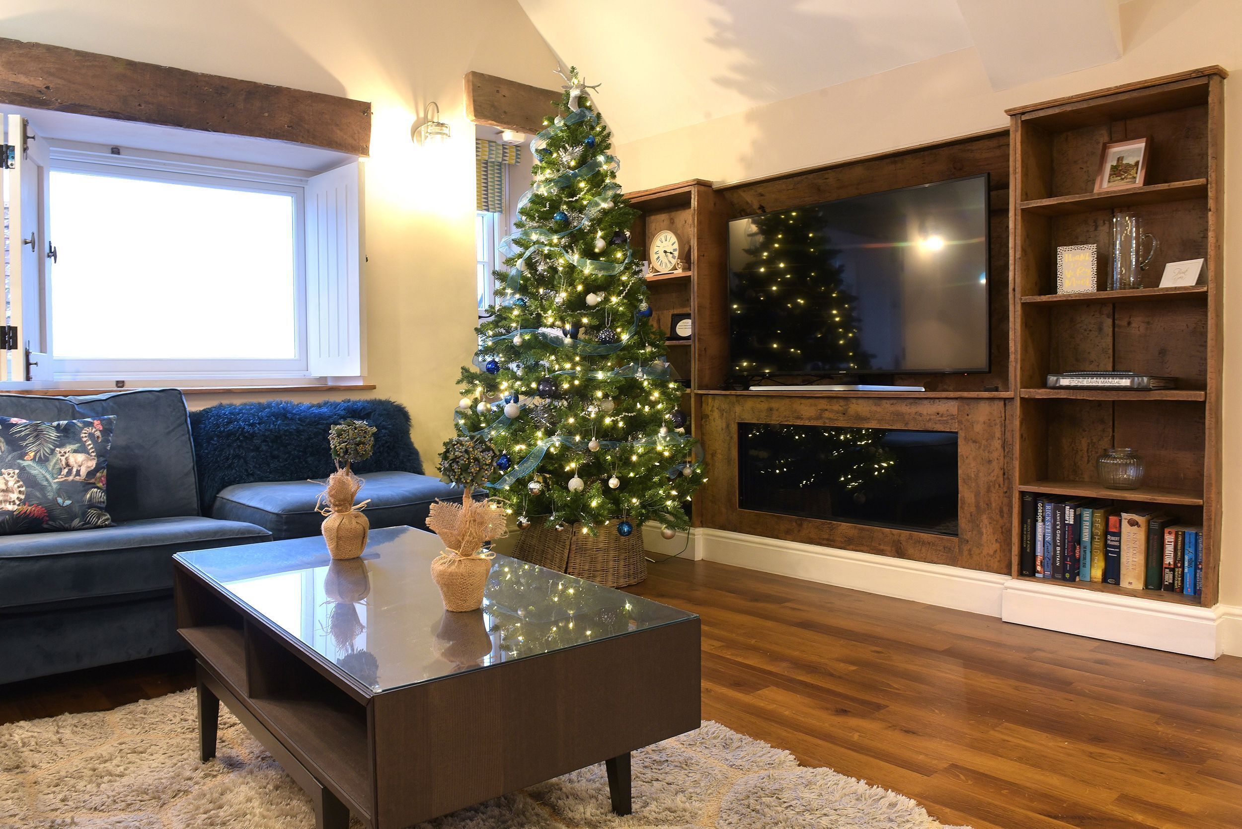 Ein Wohnzimmer mit Weihnachtsbaum, Flachbildfernseher und Bücherregal.