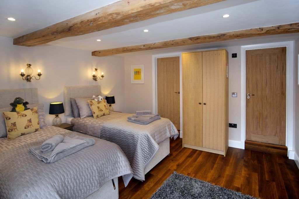 A bedroom with two beds, wooden beams, a wardrobe, and a small rug.