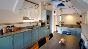 Een moderne keuken met een houten eettafel, lichtblauwe kastjes en een blauwe hanglamp.