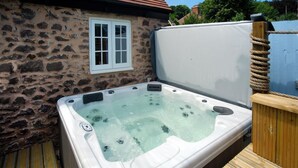 Een bubbelbad met een achtergrond van een stenen muur, een houten terras en een raam.